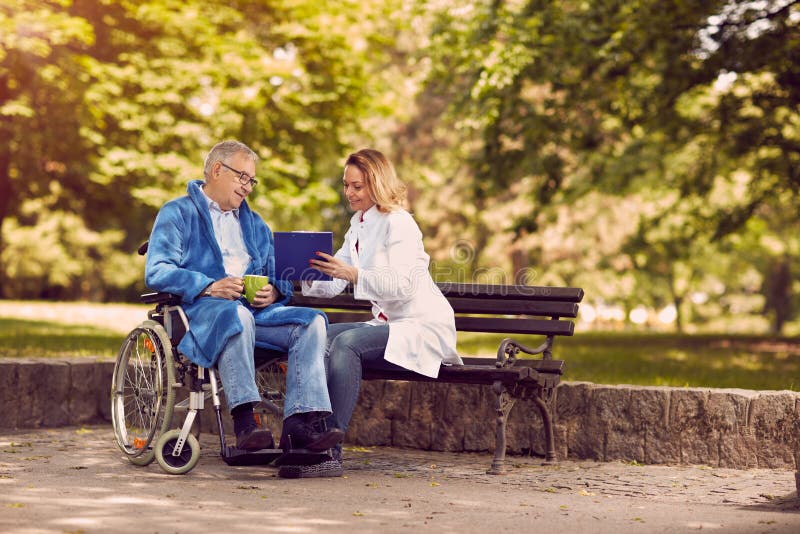 Caring nurse talking with patient in wheelchair checking up the history of the disease. Caring nurse talking with patient in wheelchair checking up the history of the disease