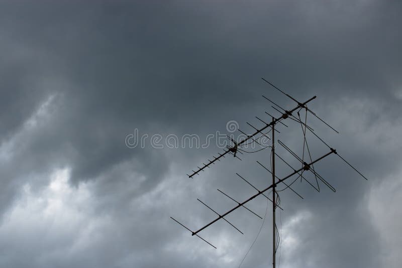 Nuvens de tempestade poderosas escuras antes da chuva contra a antena de televisão velha no telhado imagem de stock