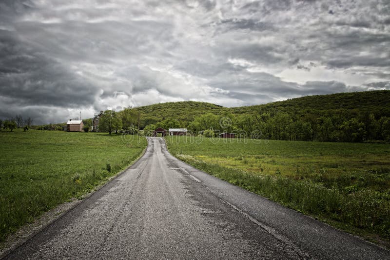 Nuvens de tempestade sobre uma estrada no campo gramíneo imagens de stock Nuvens de tempestade sobre uma estrada no campo gramíneo imagens de stock