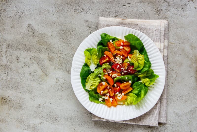 Ny plattasallad. Sund grönsallat, feta, röd sallad för körsbärsröda tomater för slutguling i den vita plattan på den lekmanna- lägenheten för ljusbetongbakgrund Rent äta, superfood, strikt vegetarian, detoxmatbegrepp Bästa sikt, lekmanna- lägenhet