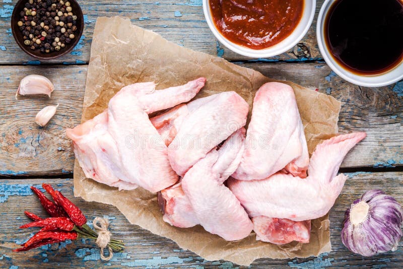 Fresh raw chicken wings, garlic, soy sauce and tomato paste and pepper on the rustic table. Fresh raw chicken wings, garlic, soy sauce and tomato paste and pepper on the rustic table