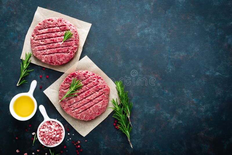 Fresh minced beef meat burgers with spices on dark background. Raw ground beef meat. Flat lay. Top view. Fresh minced beef meat burgers with spices on dark background. Raw ground beef meat. Flat lay. Top view