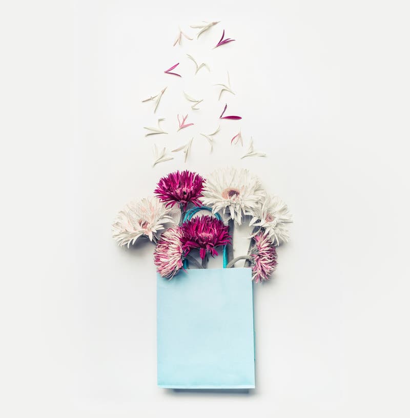 Nya älskvärda blommor i shoppingpåse för blått papper på vit skrivbords- bakgrund