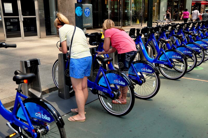 Two young women removing their rented Citibikes from a docking station on Broadway at 55th Street in NYC. Two young women removing their rented Citibikes from a docking station on Broadway at 55th Street in NYC