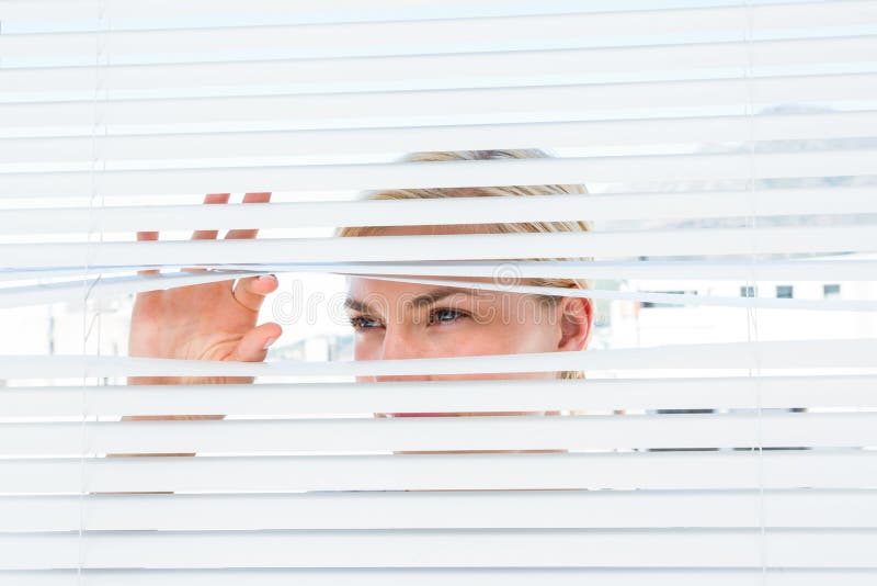 Nyfiken blond kvinna som ser till och med persiennen fotografering för bildbyråer Nyfiken blond kvinna som ser till och med persiennen fotografering för bildbyråer