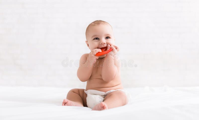 Nyfött behandla som ett barn bita röd teether i säng royaltyfria bilder Nyfött behandla som ett barn bita röd teether i säng royaltyfria bilder