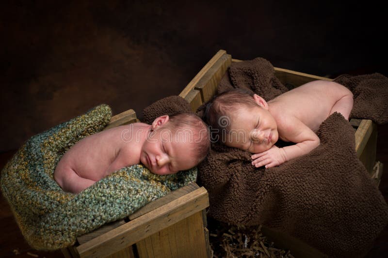 Newborn fraternal twin boys asleep on blankets in wooden crates. Newborn fraternal twin boys asleep on blankets in wooden crates.