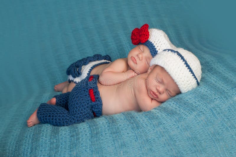 Five week old sleeping boy and girl fraternal twin newborn babies. They are wearing crocheted sailor outfits. One baby is lying on her stomach and the other is propped on top of her sister. Five week old sleeping boy and girl fraternal twin newborn babies. They are wearing crocheted sailor outfits. One baby is lying on her stomach and the other is propped on top of her sister.