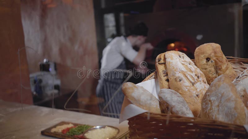 Nytt bakat bröd som ligger i korgen i förgrunden på tabellen i modernt restaurangslut upp Laga mat och ugnen med