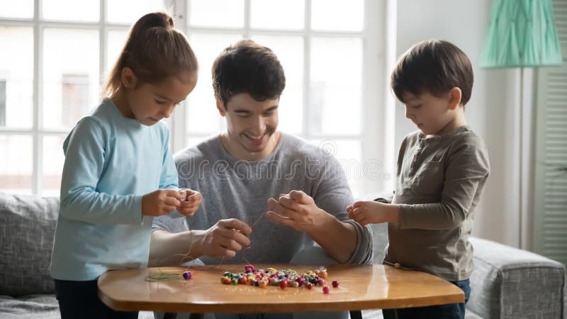 Nächster großer Vater mit den Kindern, die Spaß mit bunten Perlen haben stockfoto