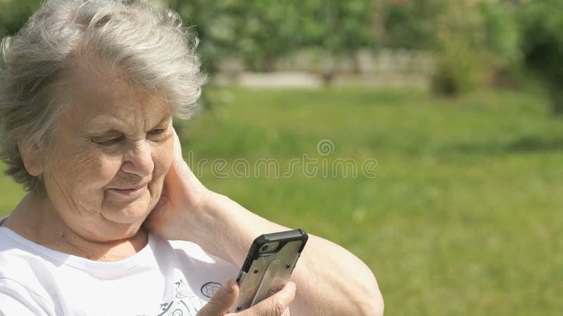 När du ler den mogna äldre kvinnan rymmer en mobiltelefon