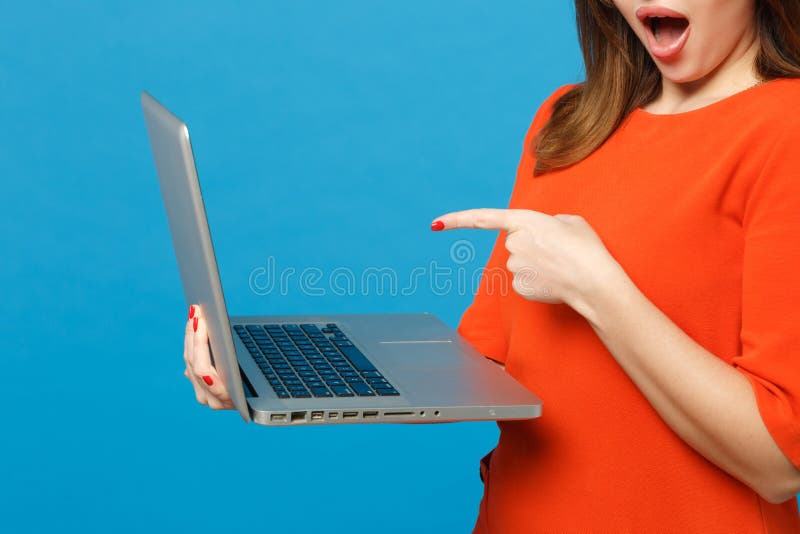 Nära beskuren kvinna med röd orange klänning i händer som pekar finger på den bärbara datorn som är isolerad på blå royaltyfri foto