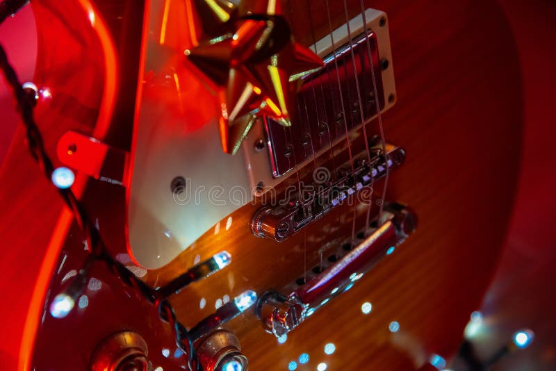 Nära en gitarr med juldekorationer. Nära en gitarr med julklackdekorationer under rött ljus