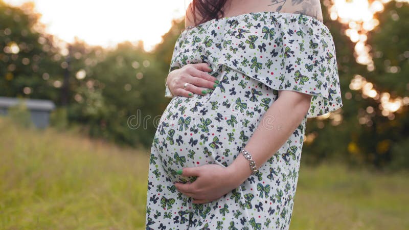Nära gravid kaukasisk kvinna i sommarklänning som placerar utomhus. attraktiv brunett som vårdar hennes tumör medan stock video