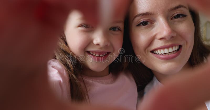 Nära vackra ansikten mamma och dotter som visar hjärttecken