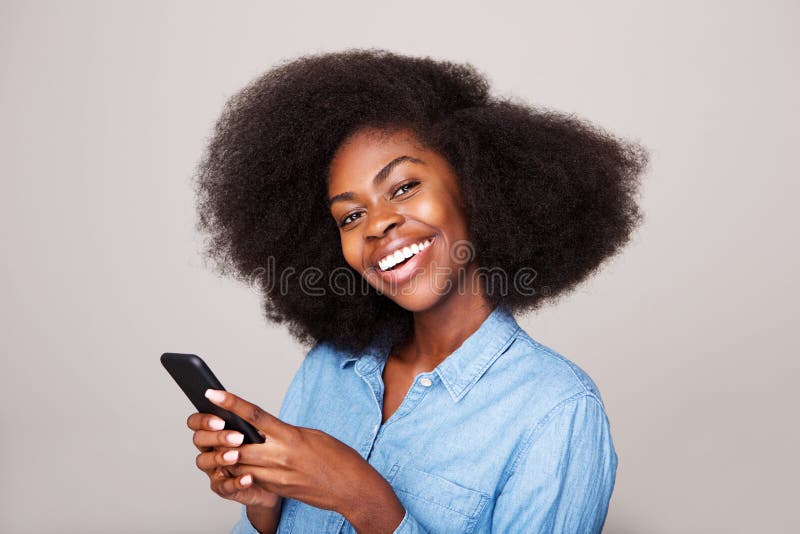 Nära övre stående av den lyckliga unga afrikansk amerikankvinnan som ler med mobiltelefonen royaltyfri foto