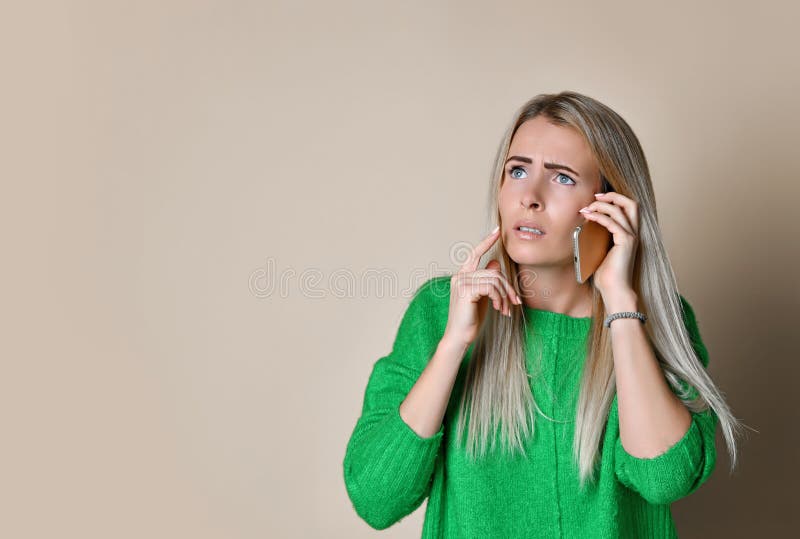 Nära övre stående av unga flickan i grön tröjablick åt sidan och att tala på den moderna digitala grejtelefonen på ljus bakgrund arkivbilder Nära övre stående av unga flickan i grön tröjablick åt sidan och att tala på den moderna digitala grejtelefonen på ljus bakgrund arkivbilder