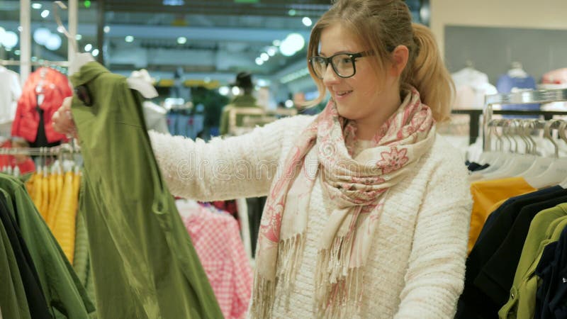 Närbild av den kvinnliga shopparen, val av modekläder av olika färger på hängare, ung attraktiv naturlig blondin