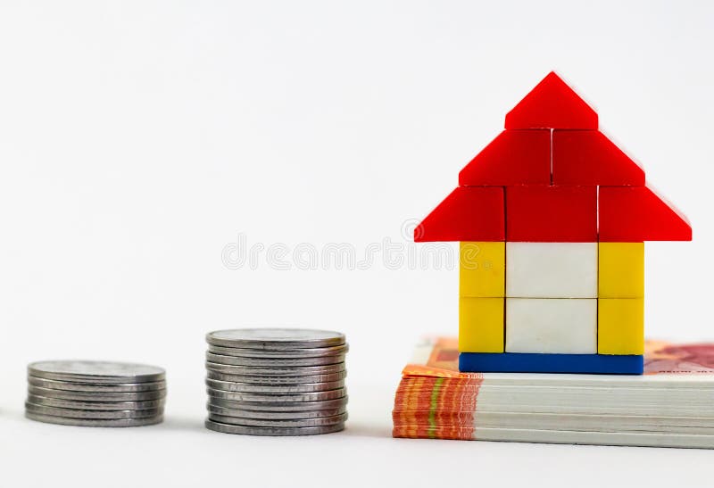 Close up shot of a lego house toy with piled coins and money notes on white background. Close up shot of a lego house toy with piled coins and money notes on white background.