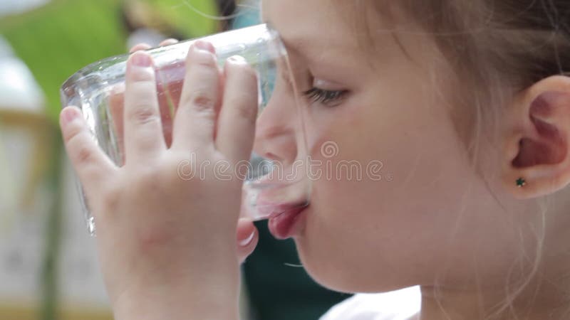Närbild av lite den gulliga flickan som dricker rent vatten från ett exponeringsglas