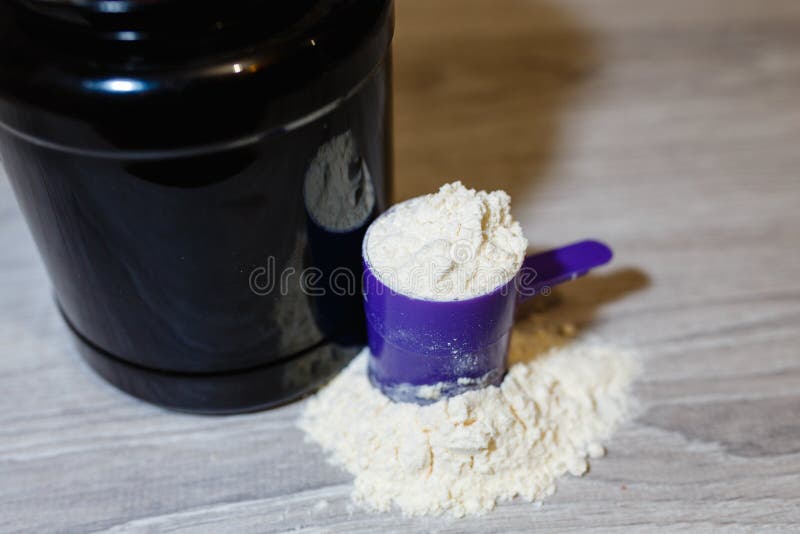 Närbildbild av ett protein för kondition och bodybuilding Skopa mycket av protein nära bankerna Svart krus med vasslakaramellprot royaltyfria foton Närbildbild av ett protein för kondition och bodybuilding Skopa mycket av protein nära bankerna Svart krus med vasslakaramellprot royaltyfria foton