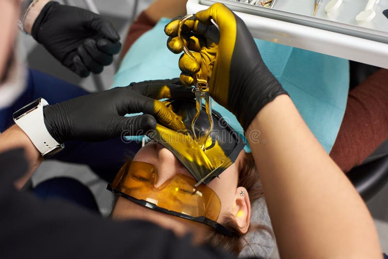 Närbilden av stomatologisten kurerar patienten med cofferdam- och sakkunnigexponeringsglas royaltyfria bilder Närbilden av stomatologisten kurerar patienten med cofferdam- och sakkunnigexponeringsglas royaltyfria bilder