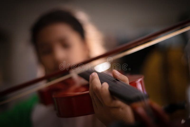 Närbildskottliten flicka som spelar fiolorkesterinstrumental med den bearbetade tappningsignalen och mörker och korn för tändande