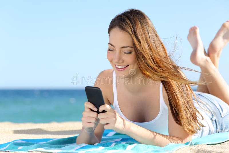 Nätt tonåringflicka som använder en smart telefon som ligger på stranden arkivbilder Nätt tonåringflicka som använder en smart telefon som ligger på stranden arkivbilder