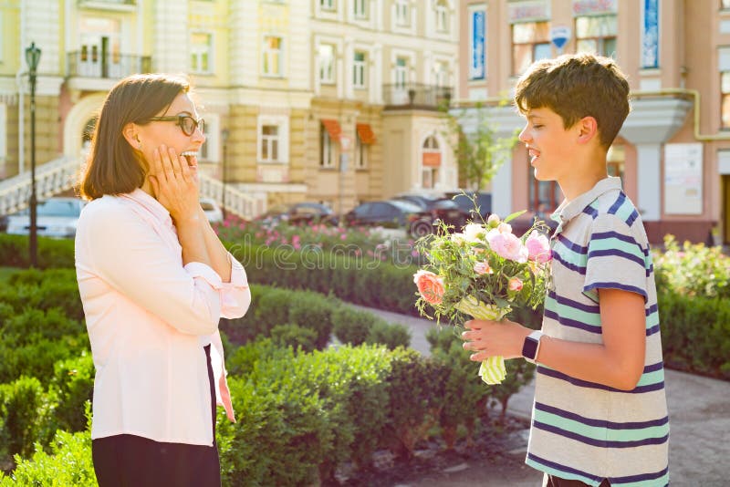 O adolescente do filho felicitou a mãe com um ramalhete da surpresa das flores foto de stock O adolescente do filho felicitou a mãe com um ramalhete da surpresa das flores foto de stock