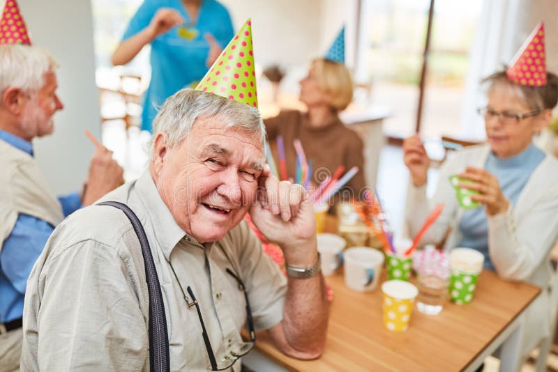 O ancião com chapéu do partido está comemorando o aniversário imagem de stock royalty free O ancião com chapéu do partido está comemorando o aniversário imagem de stock royalty free