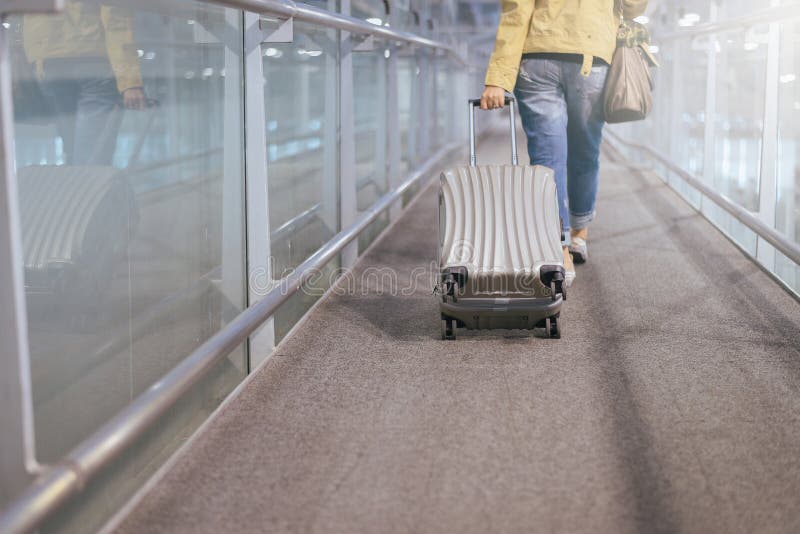 O arrasto asiático do viajante da mulher continua a mala de viagem da bagagem no corredor do aeroporto que anda às portas de part