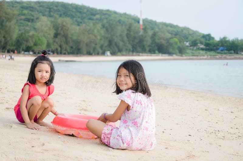 O asiático feliz do sorriso caçoa a criança tailandesa da menina que joga a areia no beac imagem de stock O asiático feliz do sorriso caçoa a criança tailandesa da menina que joga a areia no beac imagem de stock