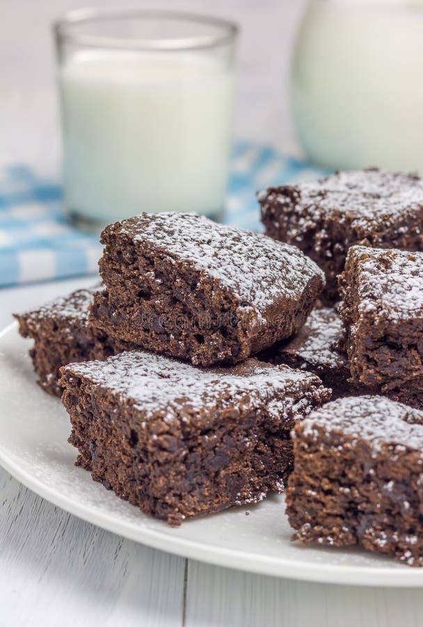 O açúcar pulverizou brownies caseiros com vidro do leite fotografia de stock O açúcar pulverizou brownies caseiros com vidro do leite fotografia de stock