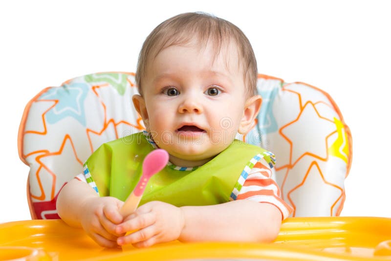 O bebê pequeno está comendo Menino da criança que senta-se com a colher na tabela foto de stock royalty free O bebê pequeno está comendo Menino da criança que senta-se com a colher na tabela foto de stock royalty free