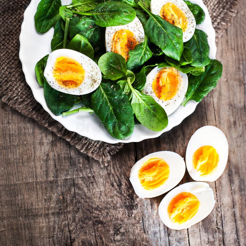 Fresh green spinach baby leaves and boiled eggs cut in a half on rustic wooden table close up image. Fresh green spinach baby leaves and boiled eggs cut in a half on rustic wooden table close up image