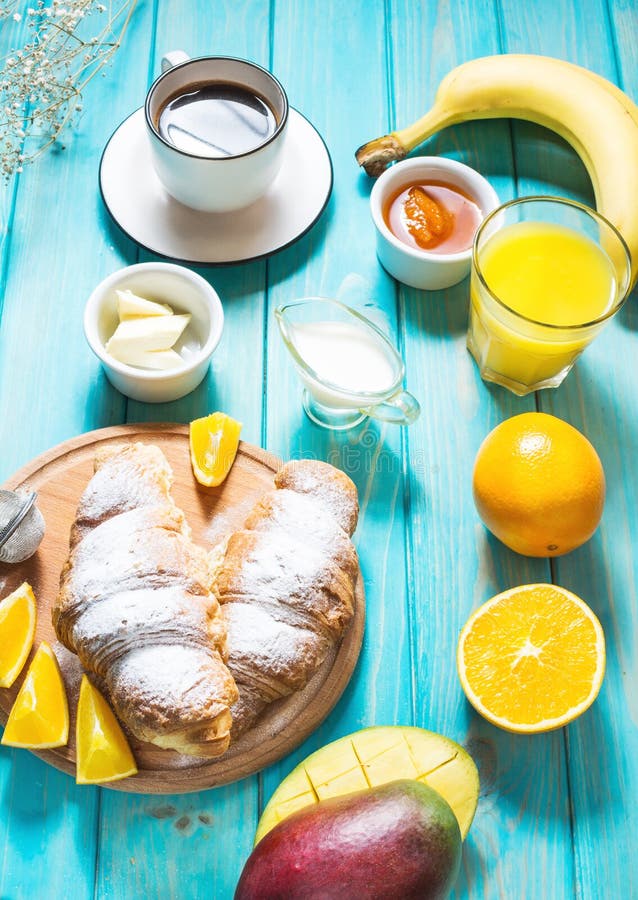 O café da manhã serviu com café, suco de laranja, croissant e frutos no fundo azul fotografia de stock royalty free O café da manhã serviu com café, suco de laranja, croissant e frutos no fundo azul fotografia de stock royalty free