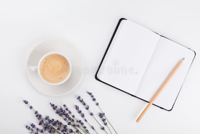 O café, o caderno limpo e a alfazema florescem na tabela branca de cima de Mesa de trabalho da mulher Modelo acolhedor do café da