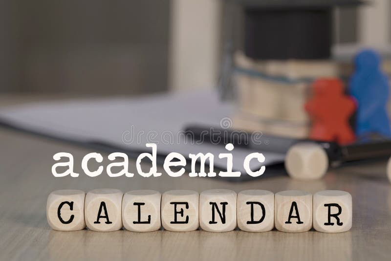 Word ACADEMIC CALENDAR composed of wooden dices. Black graduate hat and books in the background. Closeup. Word ACADEMIC CALENDAR composed of wooden dices. Black graduate hat and books in the background. Closeup