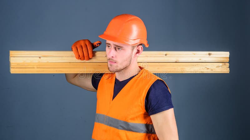 O carpinteiro, carpinteiro, construtor forte na cara séria leva o feixe de madeira no ombro Homem no capacete, capacete de segura