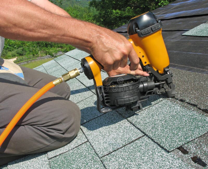 O carpinteiro usa o injetor do prego para anexar telhas do asfalto