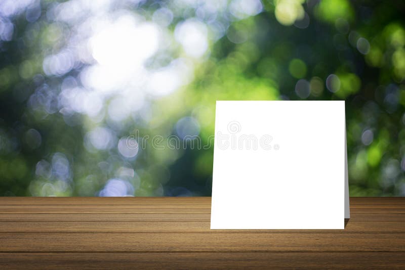 O cartão branco pôs sobre a mesa de madeira ou o assoalho de madeira sobre o fundo verde borrado da natureza da árvore uso para o fotografia de stock royalty free O cartão branco pôs sobre a mesa de madeira ou o assoalho de madeira sobre o fundo verde borrado da natureza da árvore uso para o fotografia de stock royalty free