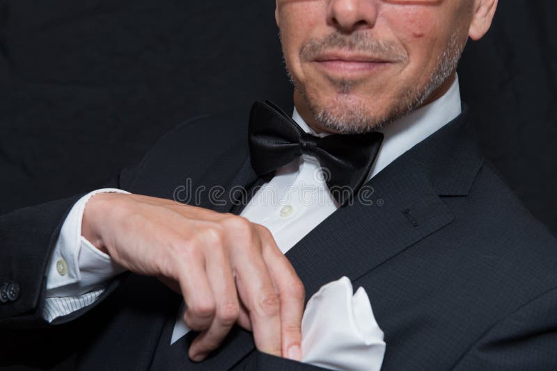 Close-up of a gentleman wearing Black Tie fixing his pocket square, horizontal. Close-up of a gentleman wearing Black Tie fixing his pocket square, horizontal.