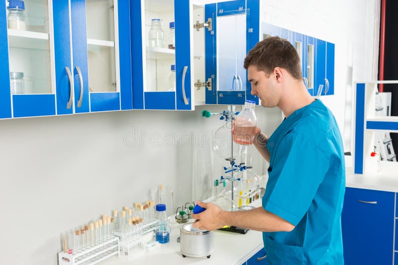 O cientista novo no uniforme está cheirando uma garrafa com produto químico s foto de stock royalty free O cientista novo no uniforme está cheirando uma garrafa com produto químico s foto de stock royalty free
