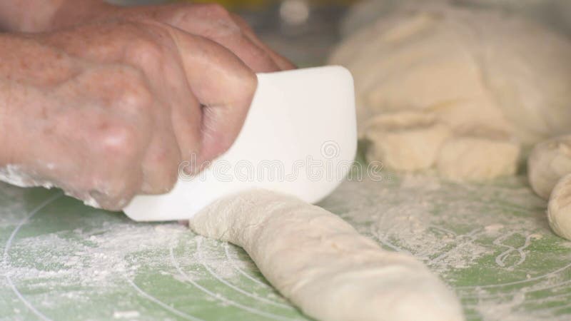 O close-up, as mãos de uma mulher idosa corta a massa com uma faca do plástico