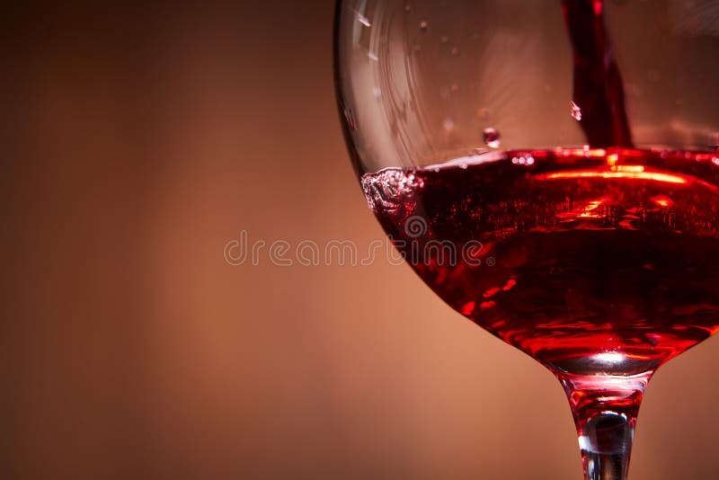 O close-up brilhantemente do vinho tinto derramou dentro o copo de vinho e o espirro abstrato contra o fundo marrom foto de stock O close-up brilhantemente do vinho tinto derramou dentro o copo de vinho e o espirro abstrato contra o fundo marrom foto de stock
