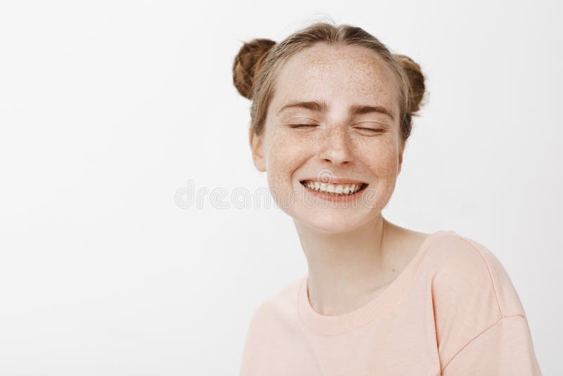O close-up disparou da fêmea macia despreocupada com bolos bonitos penteado e sardas, sorrindo alegremente com olhos fechados e fotos de stock royalty free O close-up disparou da fêmea macia despreocupada com bolos bonitos penteado e sardas, sorrindo alegremente com olhos fechados e fotos de stock royalty free