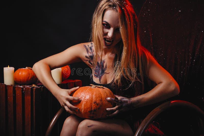 O conceito de Dia das Bruxas, vampiro da menina com os bordos vermelhos dos olhos do vermelho senta-se no ro foto de stock O conceito de Dia das Bruxas, vampiro da menina com os bordos vermelhos dos olhos do vermelho senta-se no ro foto de stock