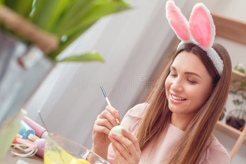 O conceito do celbration de easter da jovem mulher em casa nas orelhas de um coelho que sentam a coloração eggs pontos da pintura foto de stock royalty free O conceito do celbration de easter da jovem mulher em casa nas orelhas de um coelho que sentam a coloração eggs pontos da pintura foto de stock royalty free