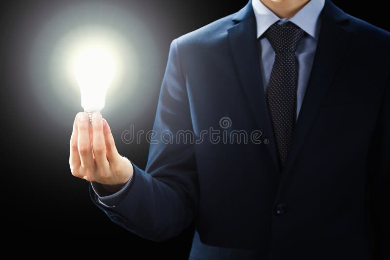 O conceito, mãos da terra arrendada do homem de negócios iluminou o sinal da ampola fotografia de stock O conceito, mãos da terra arrendada do homem de negócios iluminou o sinal da ampola fotografia de stock