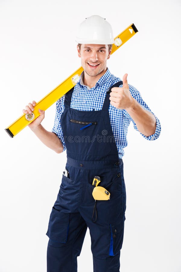 O construtor masculino de sorriso que está e que mostra manuseia acima do gesto fotografia de stock royalty free O construtor masculino de sorriso que está e que mostra manuseia acima do gesto fotografia de stock royalty free